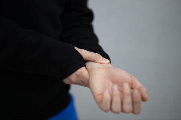 A male athlete in a hoodie and thermal underwear checks the pulse on his hand. Heart rate control close-up on a gray background.