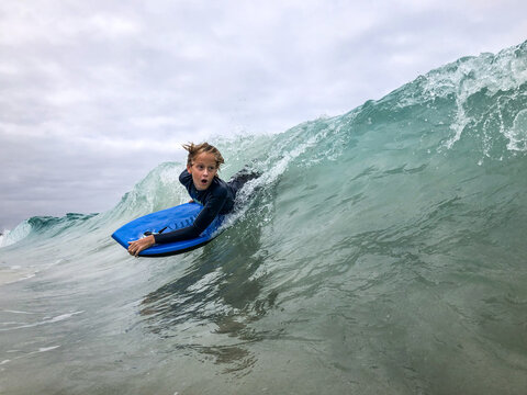 Male youth surfing wave on boogie board in ocean