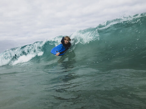 Male youth surfing wave on boogie board in ocean
