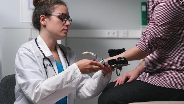 Young female doctor attach bionic robotic hand prosthesis to young disabled man