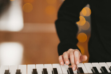 a child's hand plays the digital piano, against the background of a Christmas garland. The child...