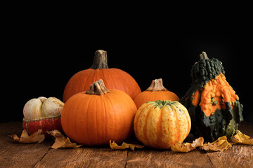 Various orange pumpkins decorated with dry leaves on a rustic wooden table. The concept of autumn, halloween, harvest.