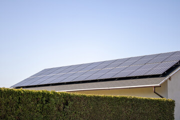Solarkollektoren auf dem Dach eines Hauses hinter einer grünen Hecke