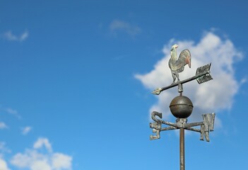 metal weather vane in the shape of a rooster to indicate the direction of the wind and the capital readings of the cardinal points on a background of the sky - obrazy, fototapety, plakaty