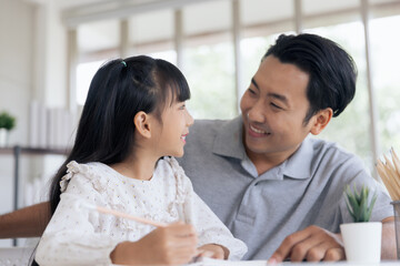 Obraz na płótnie Canvas Attractive asian father teaching little child daughter learning studying doing homework at home, Family quality time and e-learning education concept