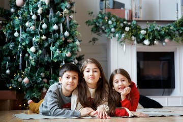 Three children a girl and a boy in festive attire are in a room decorated for the New year and Christmas.