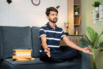 young indian student meditating before preaparing to study at home - concept of meditation, healthy...