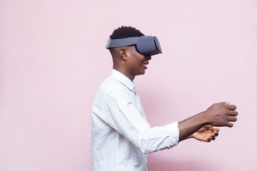 side view of young handsome black african gaming boy on vr google isolated over pink background