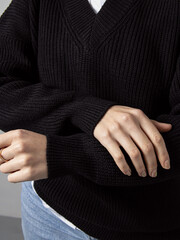 Woman in black knitted oversize pullover and blue jeans. Closeup sleeves