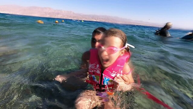 Father with daughter play in water.  kid in pink glasses and pink life vest laughing and very happy, exited. fun and joy in blue sea together. 