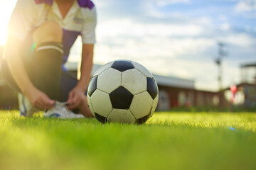 Sport man tying shoes with classic ball before playing soccer football on green grass field. Athlete sportman player and exercise concept.