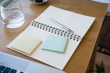 Writing on a notepad while working from home. A lap top  and plant are also on display on this brown striped working table , flat lay.