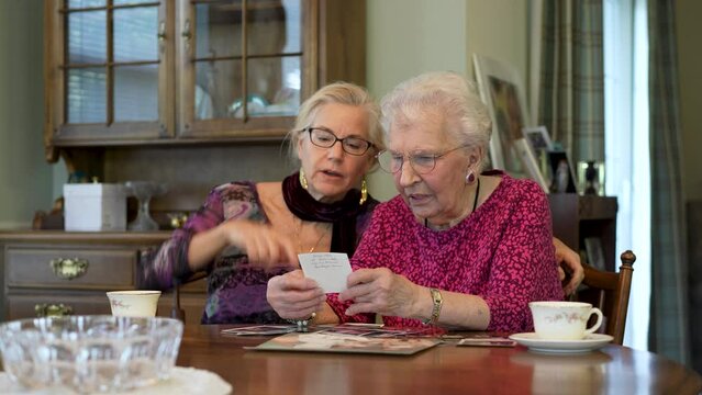 Happy elderly senior woman looks at photos with daughter. Senior woman sitting in the dining room looking at photographs with daughter. Brain training. Memory activity.