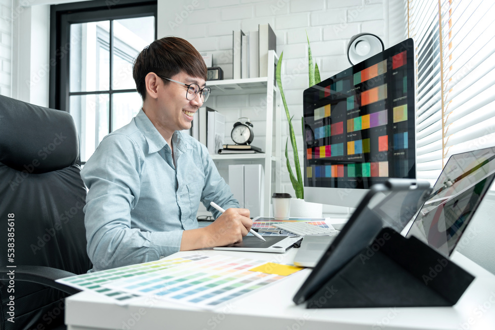 Poster male graphic designer is choosing color swatch samples on multiple screens and sketching on tablet d