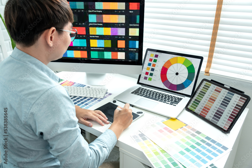 Poster male graphic designer is choosing color swatch samples on multiple screens and sketching on tablet d