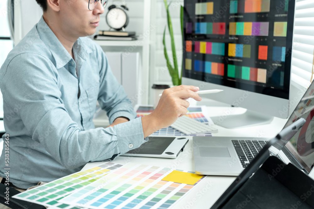 Poster male graphic designer is choosing color swatch samples on multiple screens and sketching on tablet d