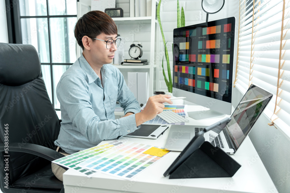 Poster male graphic designer is choosing color swatch samples on multiple screens and sketching on tablet d