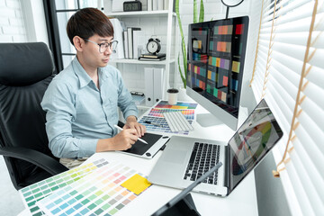 Fototapeta na wymiar Male graphic designer is choosing color swatch samples on multiple screens and sketching on tablet