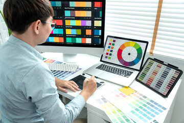 Male graphic designer is choosing color swatch samples on multiple screens and sketching on tablet...