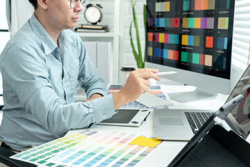 Male graphic designer is choosing color swatch samples on multiple screens and sketching on tablet digital to working graphic design with technology in modern office