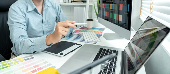 Male graphic designer is choosing color swatch samples on multiple screens and sketching on tablet digital to working graphic design with technology in modern office