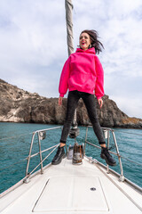 Fototapeta premium Woman standing on the nose of the yacht at a sunny summer day, breeze developing hair, beautiful sea on background