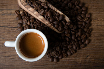 White cup of espresso with coffee beans on wooden background
