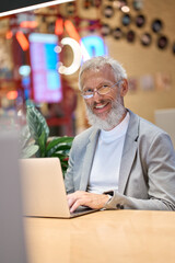 Happy smiling older senior business man office executive using laptop at work. Mature old professional businessman working late on computer typing sitting in coworking office. Vertical portrait