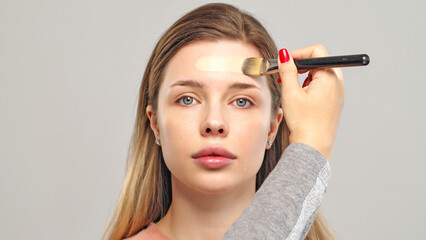 Fototapeta premium Makeup artist or stylist applies foundation or concealer to the face of the female model. Visagiste applying cosmetic foundation base on a face.
