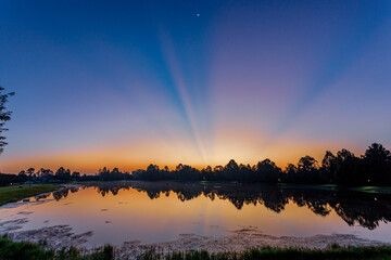 Beautiful colorful sunrise over a lake. Crepuscular rays and a pink reflection in the water