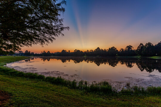 Beautiful colorful sunrise over a lake. Crepuscular rays and a pink reflection in the water