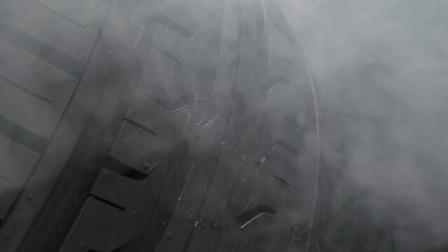 Tire Rotation in a Smoky Environment. The spinning wheel rubs against the asphalt and creates a cloud of white smoke on a black background