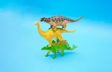 Three dinosaurs stand on each other on a blue background. Plastic toys.