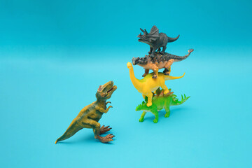 Four dinosaurs stand on each other on a blue background. Ankylosaurus, Brachiosaurus, Stegosaurus and Triceratops against T-Rex. Blue background. Minimal design and concept..Plastic toys.