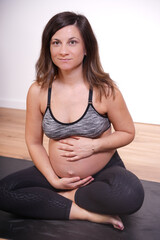 beautiful 30s-40s pregnant woman exercising yoga and touching belly