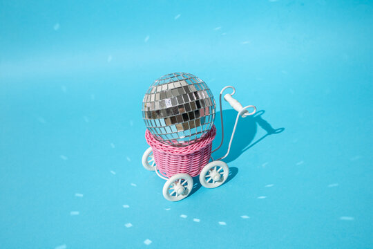 Toy pink shopping cart with disco ball on a blue background.