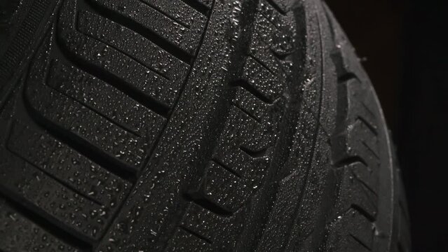 Wet Tire Tread on Black Background. The surface of a car tire covered with shiny drops of water floats slowly in front of the camera close-up on a black background