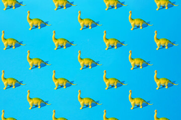 Fototapeta na wymiar Yellow green plastic toy Brachiosaurus dinosaur on a blue background. Minimal pattern.