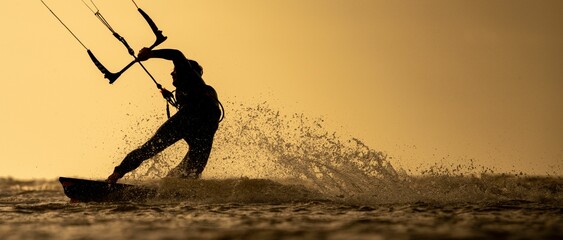 Silhouette of a person kitesurfing with splashes of water under a clear yellow-brown sky at sea