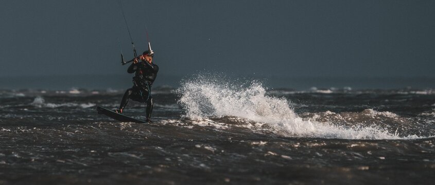Man kitesurfing under a clear dark sky with waves splashing behind him in the sea