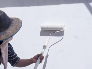 A worker is painting the walls of the house with a primer using a paint roller.