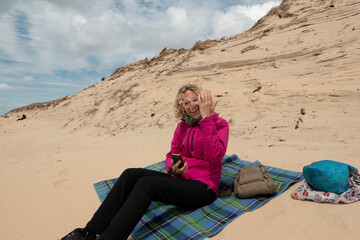 Fototapeta na wymiar woman sitting on the beach picknik in the sand warm dressed with smartphone