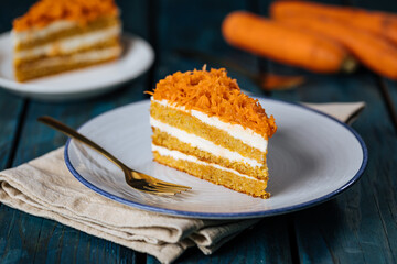 Carrot cake with cream cheese in layers and carrots on top on a  blue and white background with...