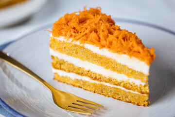 Carrot cake with cream cheese in layers and carrots on top on a  blue and white background with carrots in blurry background