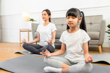 Obraz premium Asian young mother and her daughter setting prepare to yoga and meditation pose together on yoga mat in living room at home. Fitness lifestyle.