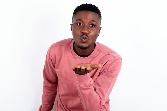 young handsome man wearing pink sweater over white background looking at the camera blowing a kiss with hand on air being lovely. Love expression.