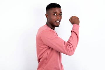 young handsome man wearing pink sweater over white background,  showing muscles after workout. Health and strength concept.