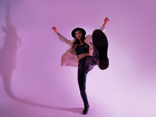 Stylish young woman in a black hat and jacket. posing in the studio with pink light on the background