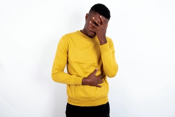young handsome man wearing yellow sweater over white background making facepalm gesture while...