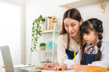 Happy asian mother and daughter having video call, waving and smiling at laptop screen, sitting in kitchen .School girl using computer, having online lesson while coronavirus pandemic.